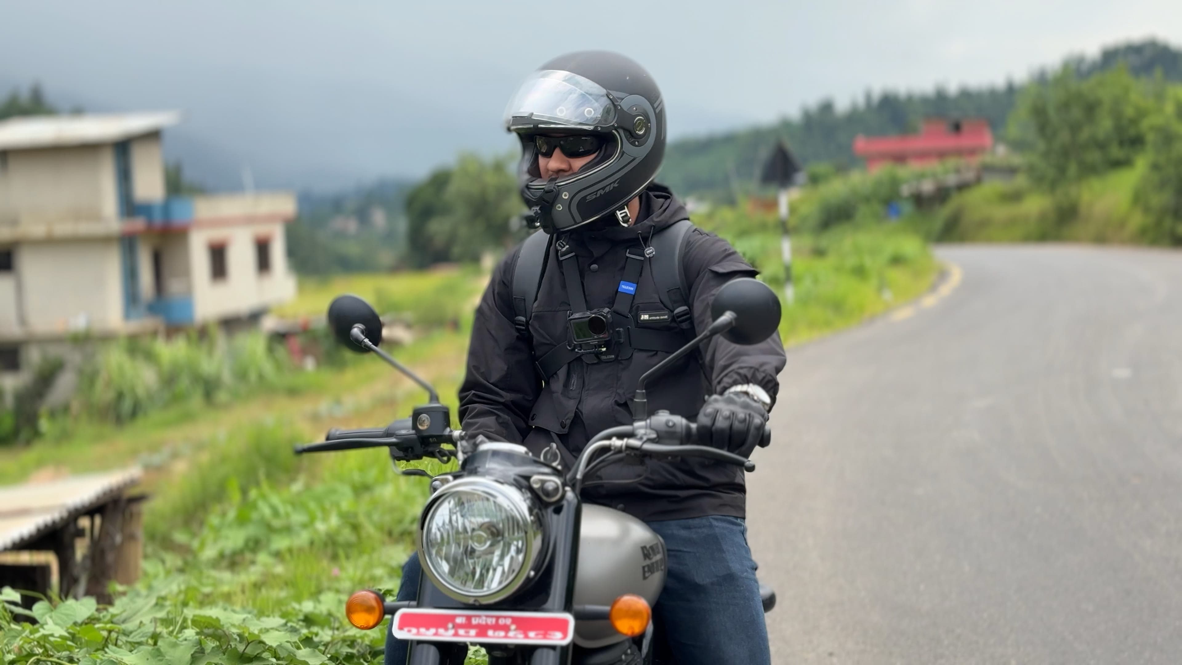 Ranjit in helmet and riding jacket on his Royal Enfield Classic 350, stopped on a hill road above Kathmandu